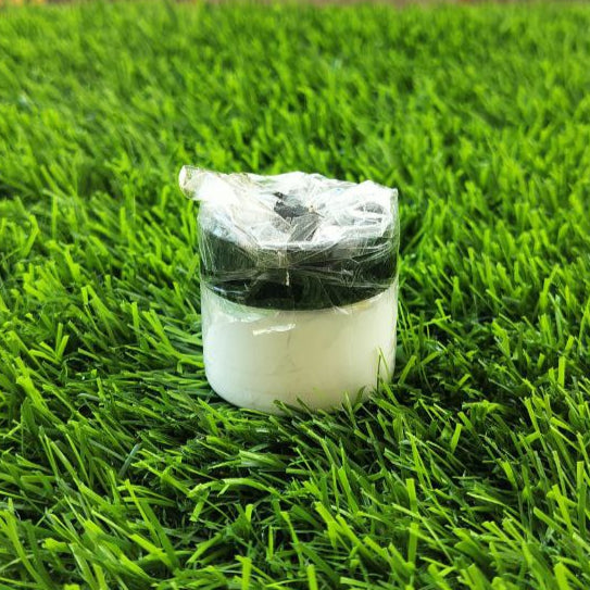 Small white container with a black lid on artificial grass with a patterned wall in the background